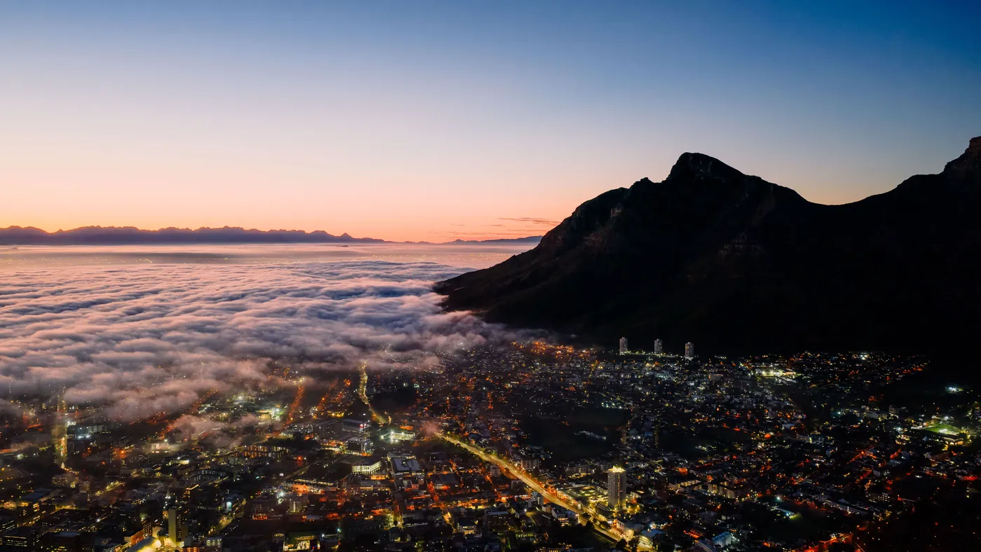 Cloud cover rolling in over Cape Town at twilight, with the lit city below the mountain
