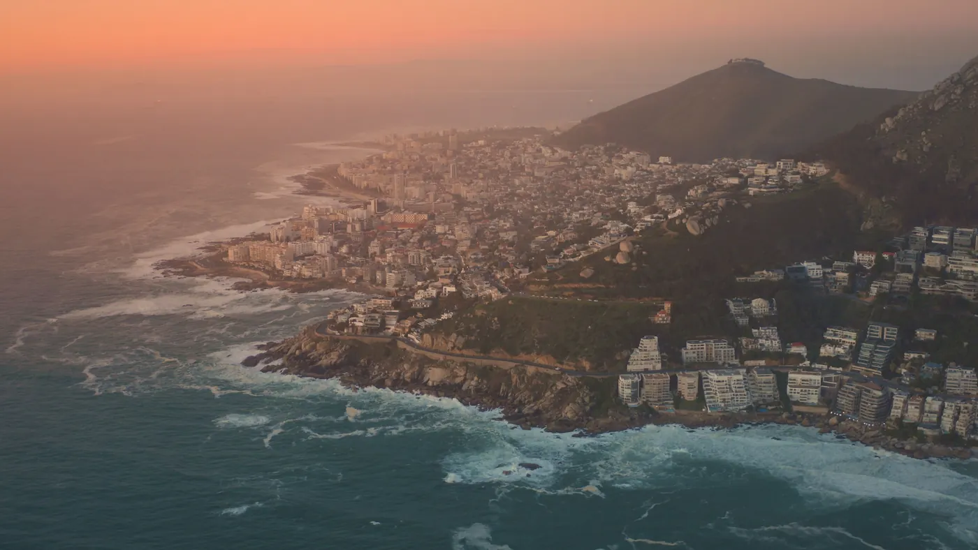 Aerial view of the Cape Town coastline at sunset, with surf breaking along the headland