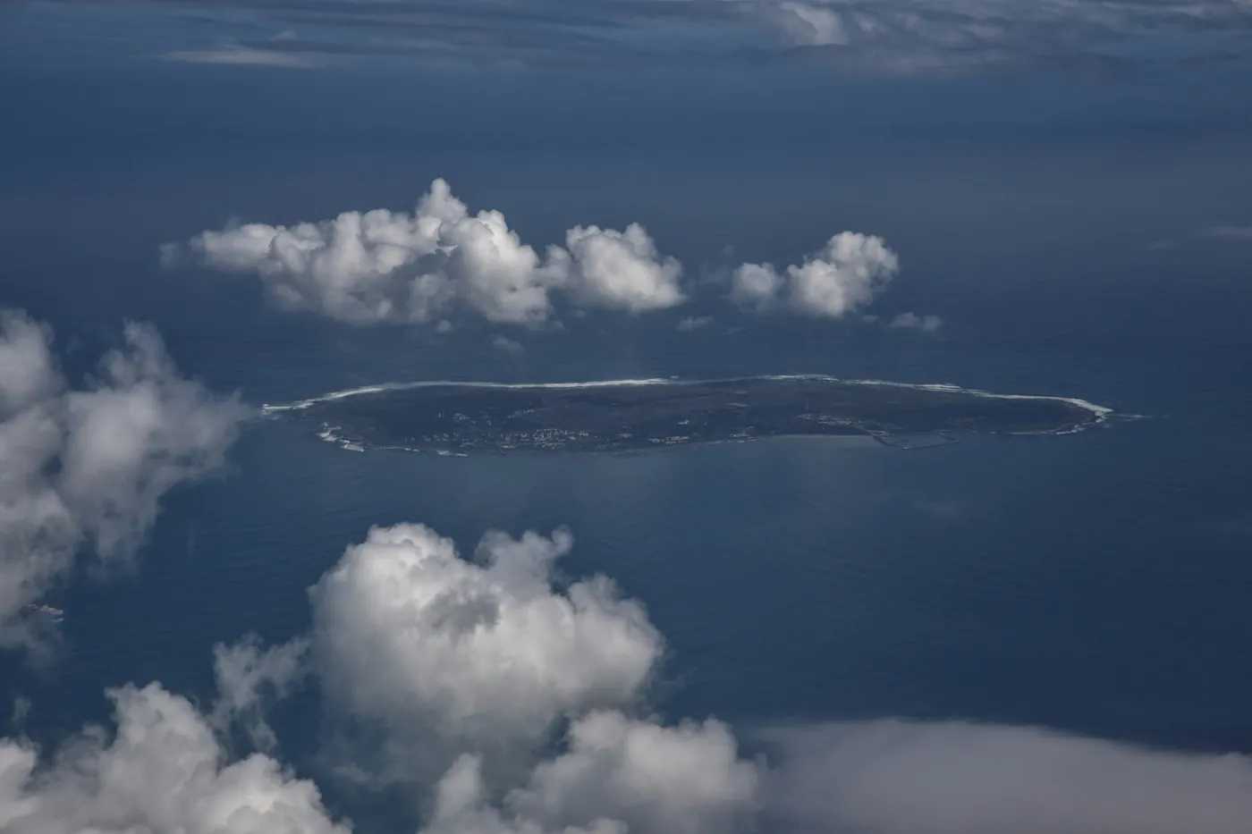 Robben Island seen from the air, low and flat in Table Bay between banks of cloud
