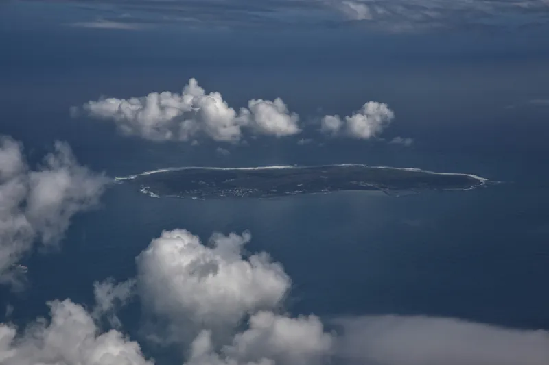 Robben Island seen from the air, low and flat in Table Bay between banks of cloud